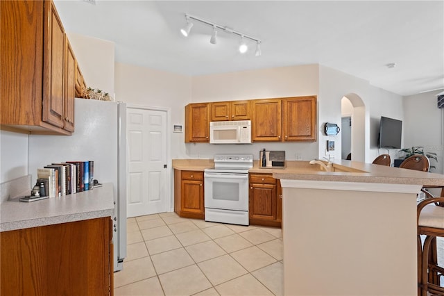 kitchen with sink, kitchen peninsula, white appliances, a breakfast bar area, and light tile patterned flooring