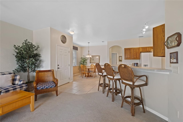 kitchen with white refrigerator with ice dispenser, kitchen peninsula, light colored carpet, decorative light fixtures, and a kitchen bar