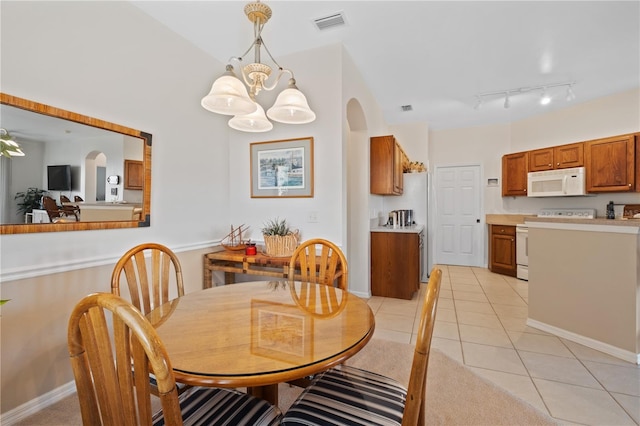 tiled dining room featuring track lighting, an inviting chandelier, and lofted ceiling