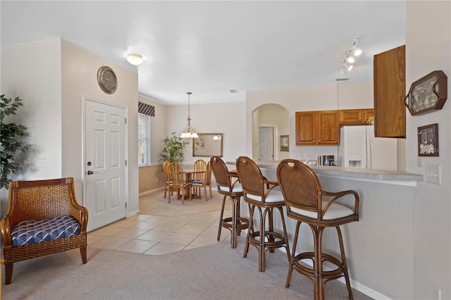 kitchen featuring kitchen peninsula, a kitchen breakfast bar, white refrigerator with ice dispenser, pendant lighting, and light tile patterned flooring