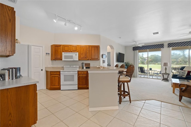 kitchen with white appliances, light carpet, a kitchen breakfast bar, ceiling fan, and kitchen peninsula