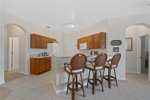 kitchen with a kitchen bar, light carpet, rail lighting, and white appliances