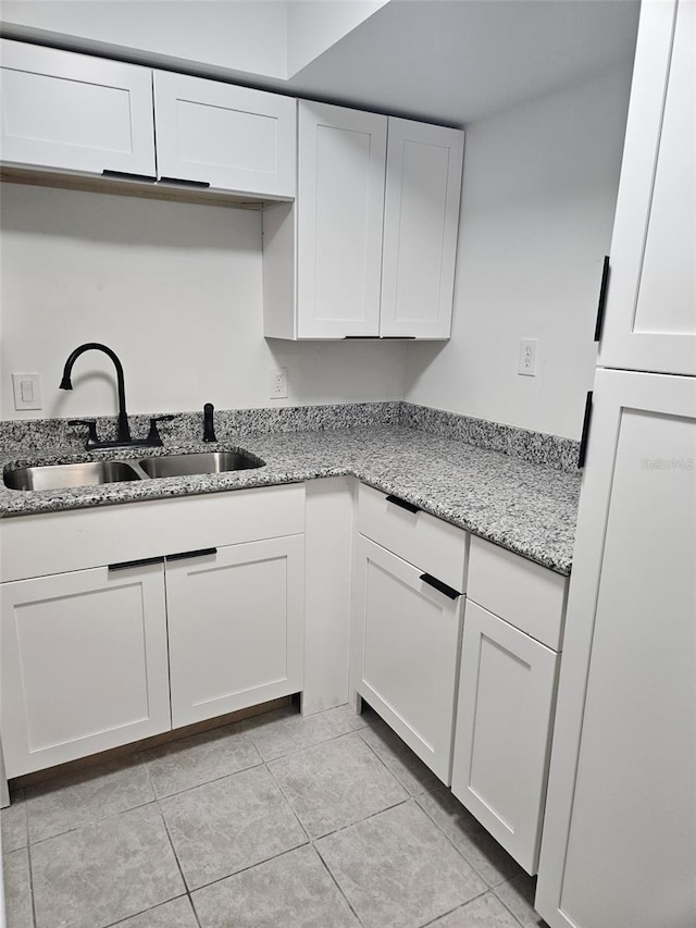 kitchen with light stone countertops, light tile patterned floors, white cabinets, and sink