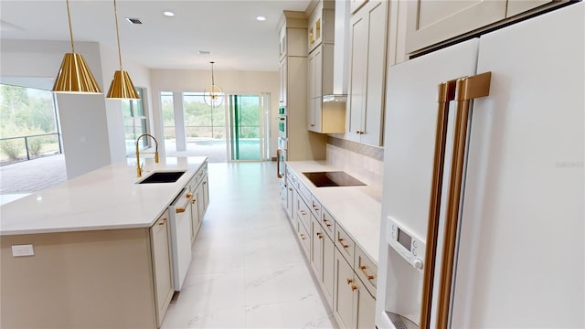 kitchen featuring high end white refrigerator, a center island with sink, decorative light fixtures, and sink