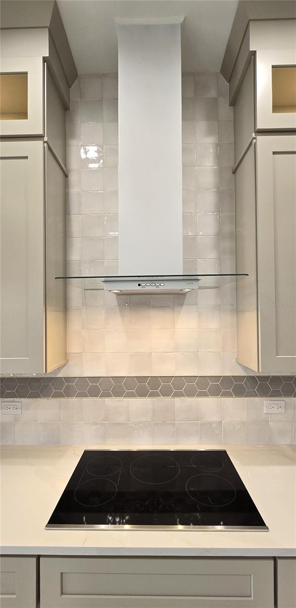 kitchen featuring gray cabinetry, black electric stovetop, tasteful backsplash, and wall chimney exhaust hood