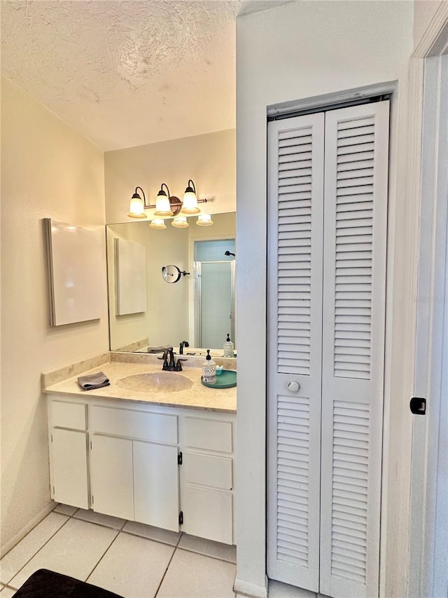 bathroom with tile patterned floors, walk in shower, a textured ceiling, and vanity