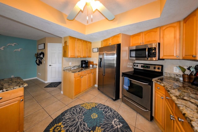 kitchen with stainless steel appliances, light tile floors, dark stone counters, ceiling fan, and tasteful backsplash