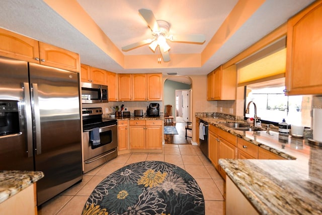 kitchen featuring ceiling fan, sink, stainless steel appliances, light tile floors, and a raised ceiling