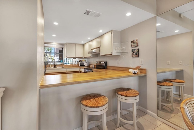 kitchen featuring a breakfast bar area, light tile floors, sink, kitchen peninsula, and electric stove