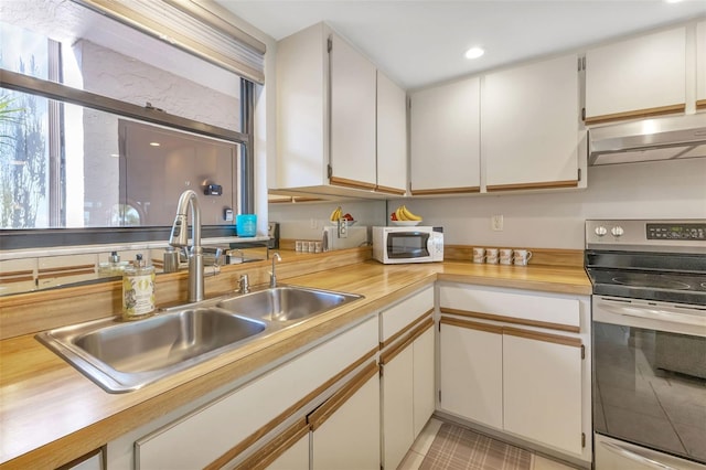 kitchen featuring sink, light tile floors, white cabinets, stainless steel electric range oven, and wall chimney range hood