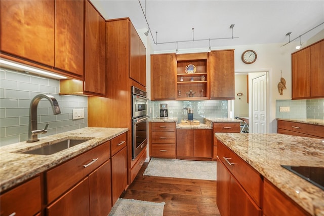 kitchen with double oven, tasteful backsplash, light stone counters, dark hardwood / wood-style floors, and sink