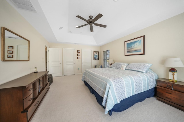 carpeted bedroom featuring a raised ceiling, multiple closets, and ceiling fan