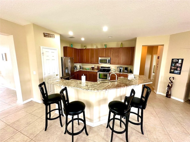 kitchen featuring a kitchen breakfast bar, a textured ceiling, stainless steel appliances, a spacious island, and light tile patterned floors