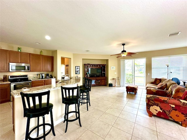 kitchen with a kitchen bar, light stone counters, light tile patterned floors, and appliances with stainless steel finishes