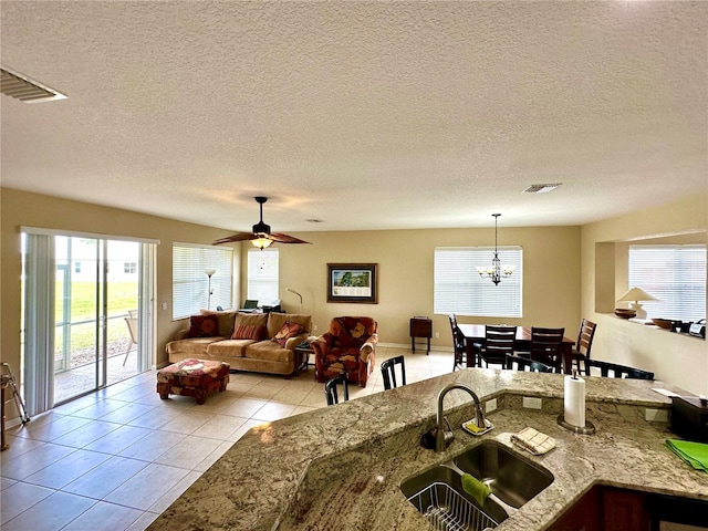 kitchen featuring ceiling fan with notable chandelier, a textured ceiling, sink, hanging light fixtures, and light tile patterned flooring