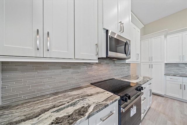 kitchen with white cabinetry, light stone counters, stainless steel appliances, and light hardwood / wood-style floors