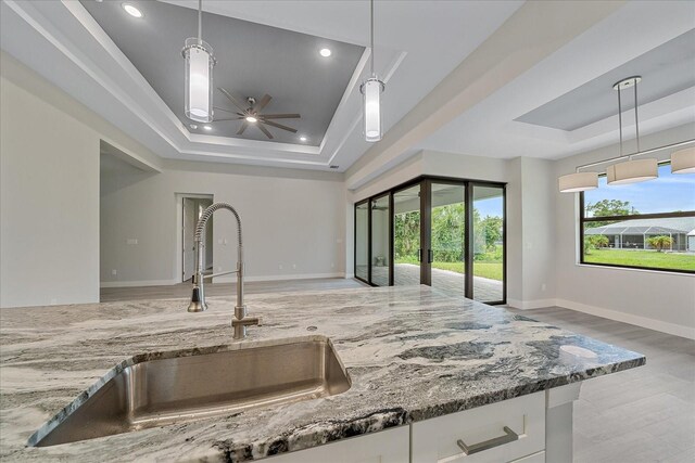 kitchen featuring a tray ceiling, white cabinets, sink, and stone counters