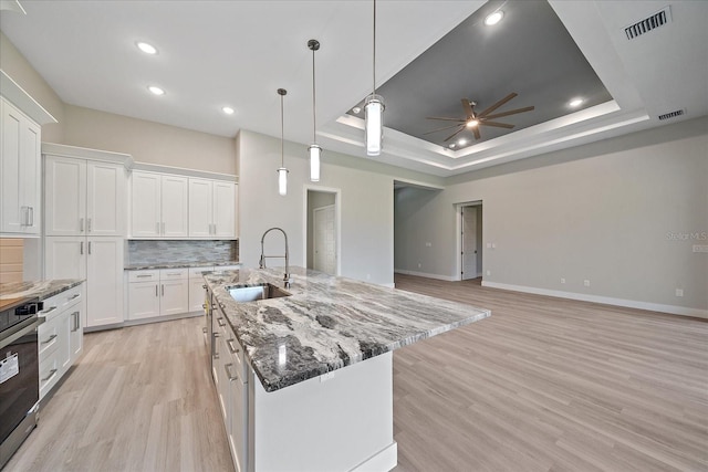 kitchen with light wood-type flooring, a raised ceiling, white cabinetry, and ceiling fan