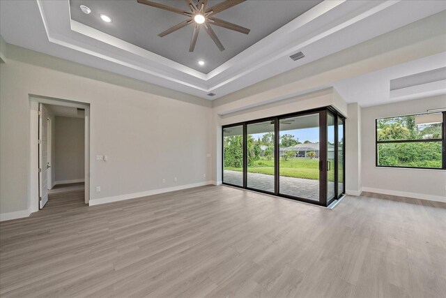 empty room with a tray ceiling, light hardwood / wood-style flooring, and ceiling fan