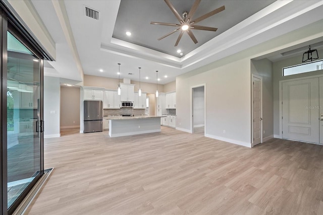 unfurnished living room with light wood-type flooring, a raised ceiling, a healthy amount of sunlight, and ceiling fan