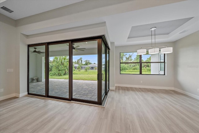 doorway to outside featuring a raised ceiling, ceiling fan, and light wood-type flooring