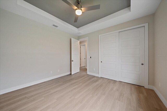 unfurnished bedroom featuring a closet, a tray ceiling, light hardwood / wood-style floors, and ceiling fan