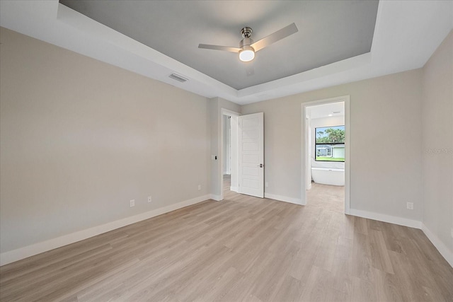 spare room featuring a tray ceiling, light hardwood / wood-style flooring, and ceiling fan