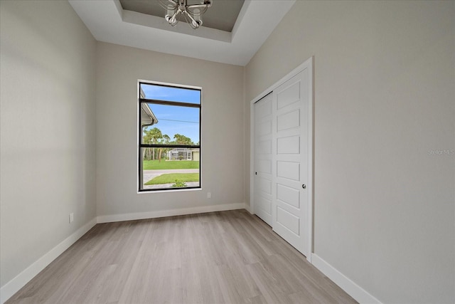 unfurnished bedroom with a notable chandelier, a closet, a tray ceiling, and light hardwood / wood-style floors