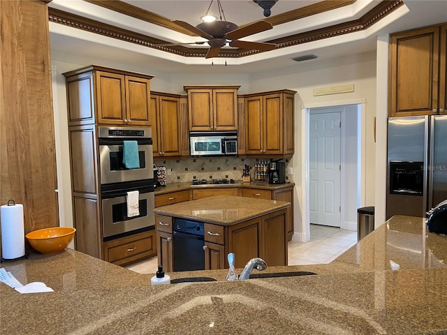 kitchen featuring a tray ceiling, a kitchen island, ceiling fan, and stainless steel appliances