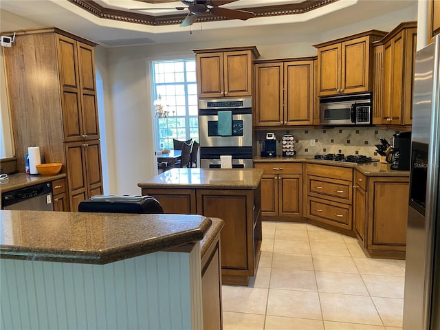 kitchen with ceiling fan, backsplash, appliances with stainless steel finishes, a tray ceiling, and a center island