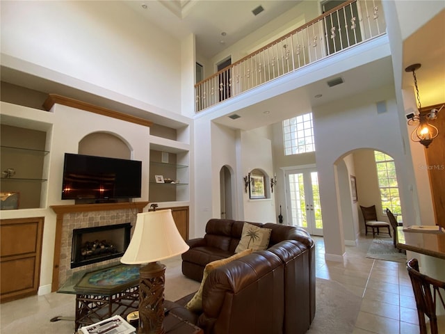 tiled living room featuring a towering ceiling, a tiled fireplace, and built in features