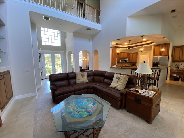 living room featuring french doors, light tile patterned flooring, a raised ceiling, and a towering ceiling