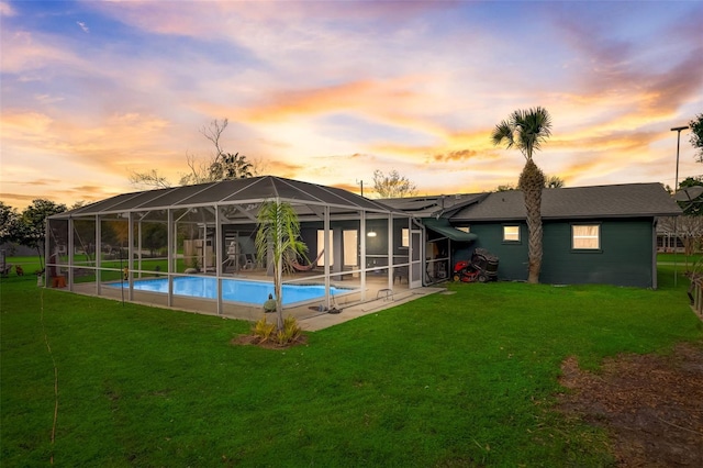 back house at dusk featuring a lawn, a patio area, and glass enclosure