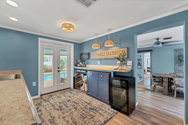 kitchen with blue cabinetry, pendant lighting, french doors, ornamental molding, and light hardwood / wood-style flooring