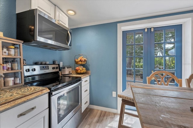 kitchen featuring white cabinets, appliances with stainless steel finishes, ornamental molding, and light hardwood / wood-style flooring