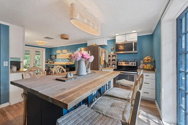 kitchen with hanging light fixtures, white cabinets, stainless steel appliances, butcher block counters, and light wood-type flooring