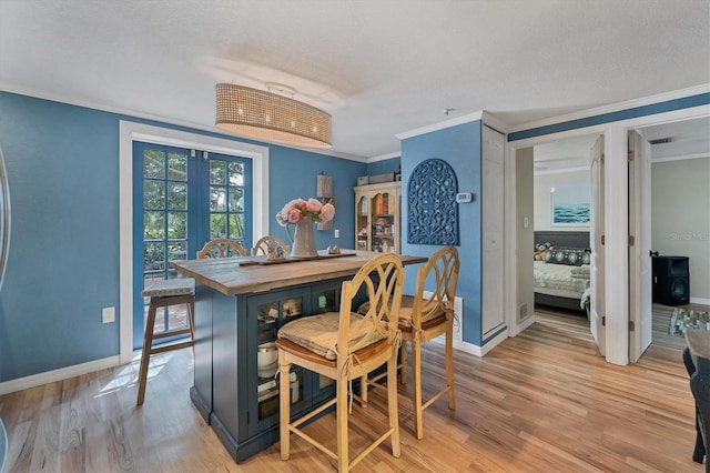 dining space featuring a textured ceiling, light hardwood / wood-style flooring, french doors, and crown molding