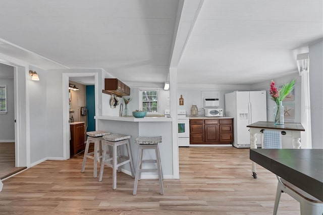 kitchen with light hardwood / wood-style floors, white appliances, and a breakfast bar