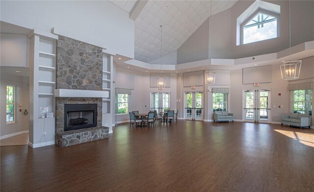 unfurnished living room featuring a stone fireplace, an inviting chandelier, a towering ceiling, and dark wood-type flooring