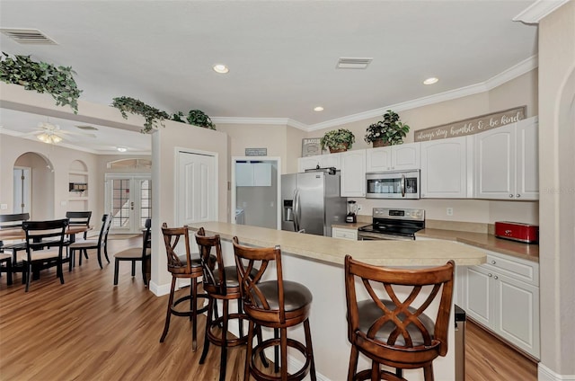 kitchen with appliances with stainless steel finishes, light hardwood / wood-style flooring, ceiling fan, white cabinetry, and a kitchen breakfast bar