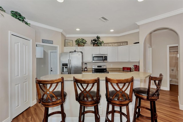 kitchen featuring appliances with stainless steel finishes, light hardwood / wood-style floors, white cabinets, and a kitchen bar