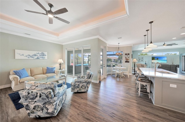 living room featuring ceiling fan, sink, ornamental molding, a tray ceiling, and dark wood-type flooring