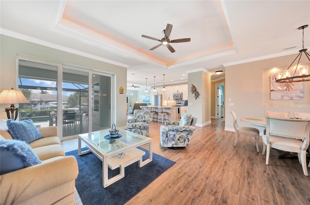 living room featuring light hardwood / wood-style floors, ornamental molding, ceiling fan with notable chandelier, and a tray ceiling