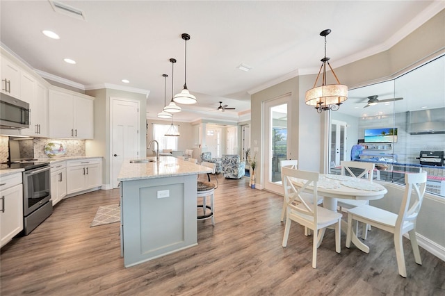 kitchen featuring backsplash, a kitchen island with sink, appliances with stainless steel finishes, light wood-type flooring, and pendant lighting