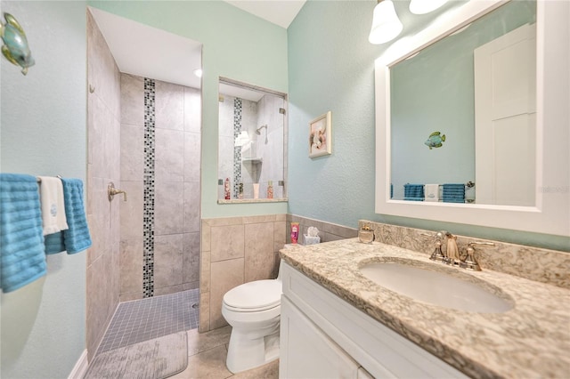 bathroom with toilet, tile floors, vanity, and tiled shower