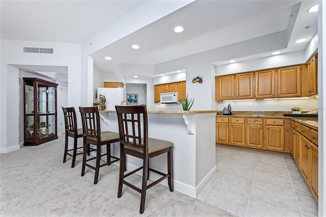 kitchen with light stone countertops, white appliances, a breakfast bar area, and light carpet