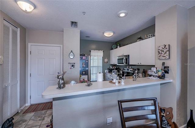 kitchen with light tile flooring, appliances with stainless steel finishes, kitchen peninsula, and white cabinetry