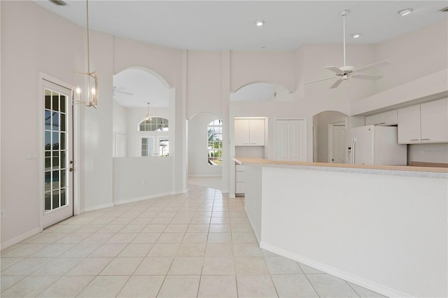 kitchen featuring white refrigerator with ice dispenser, a high ceiling, light tile patterned floors, decorative light fixtures, and white cabinetry