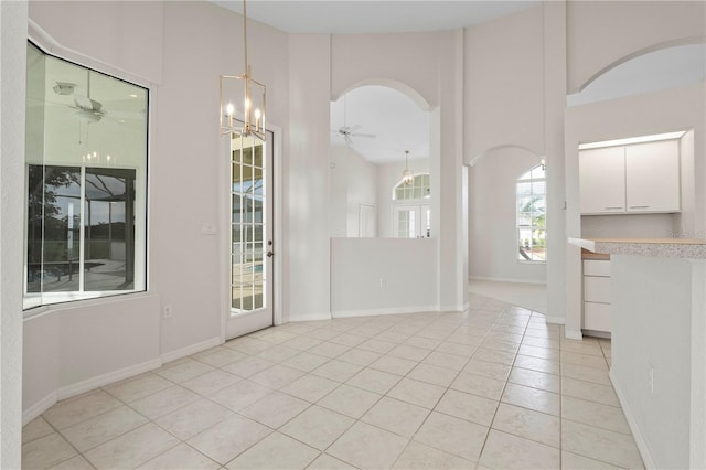 unfurnished dining area featuring light tile patterned floors, ceiling fan with notable chandelier, and a high ceiling