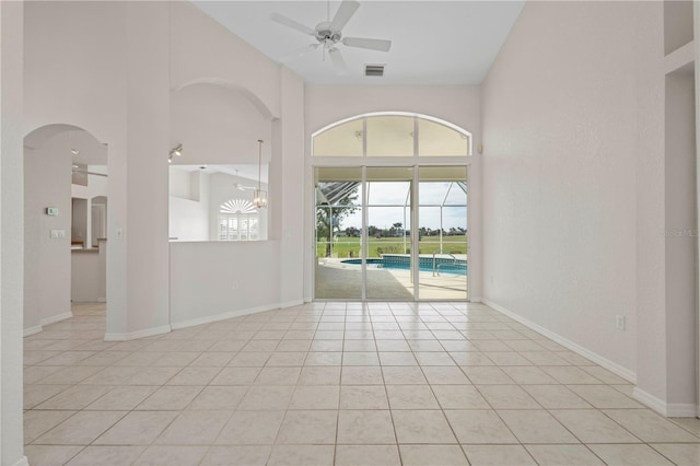 tiled empty room featuring ceiling fan and a towering ceiling